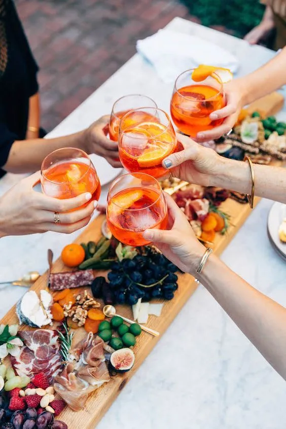 Verres de spritz levés au-dessus d'une grande planche apéro